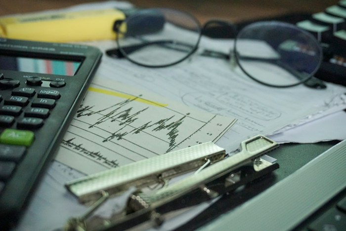 A desk with a calculator, printed charts and a pair of glasses