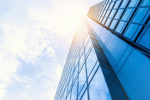 A glass office tower rising into a bright sky