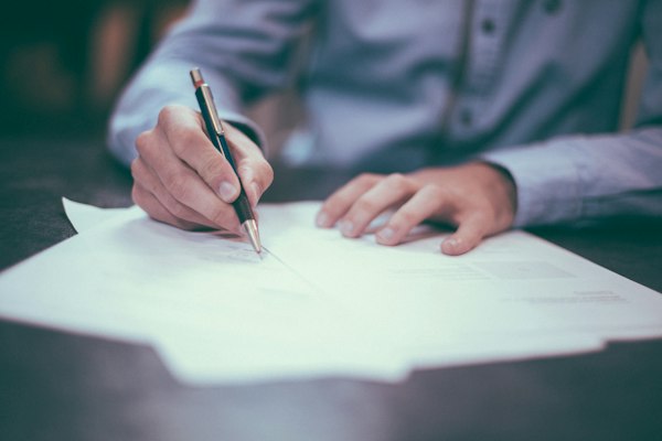 A hand signing a document with a pen