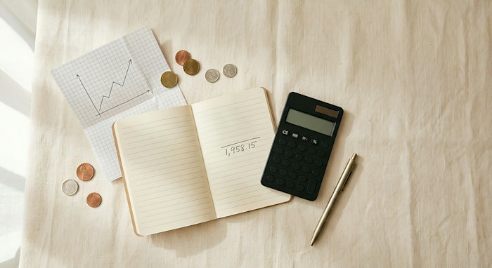 An open notebook, a calculator, a pen, coins and a sketched graph on a light table
