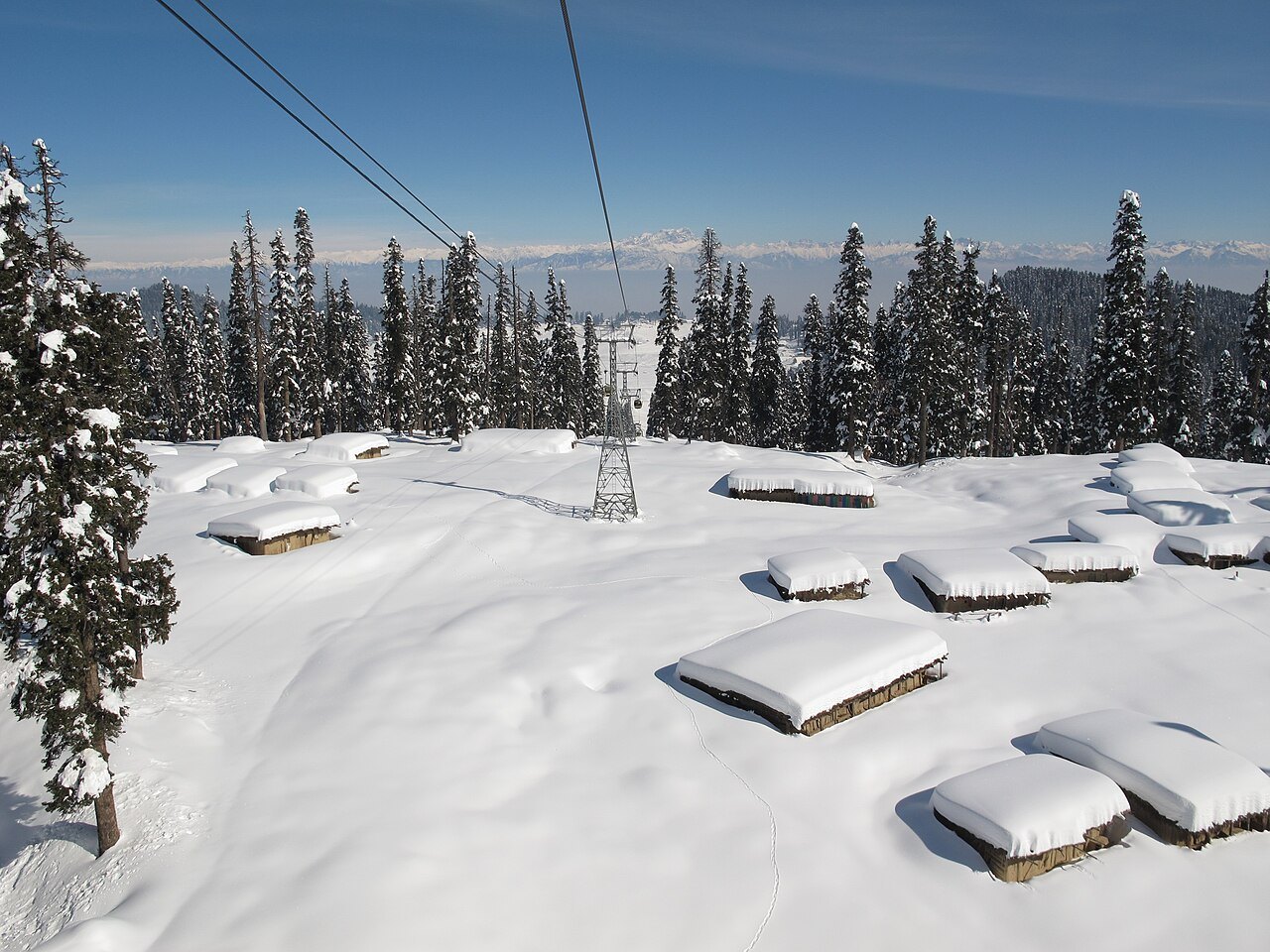 Deep fresh snow on huts and pine trees below the Gulmarg gondola in Kashmir, under a clear sky