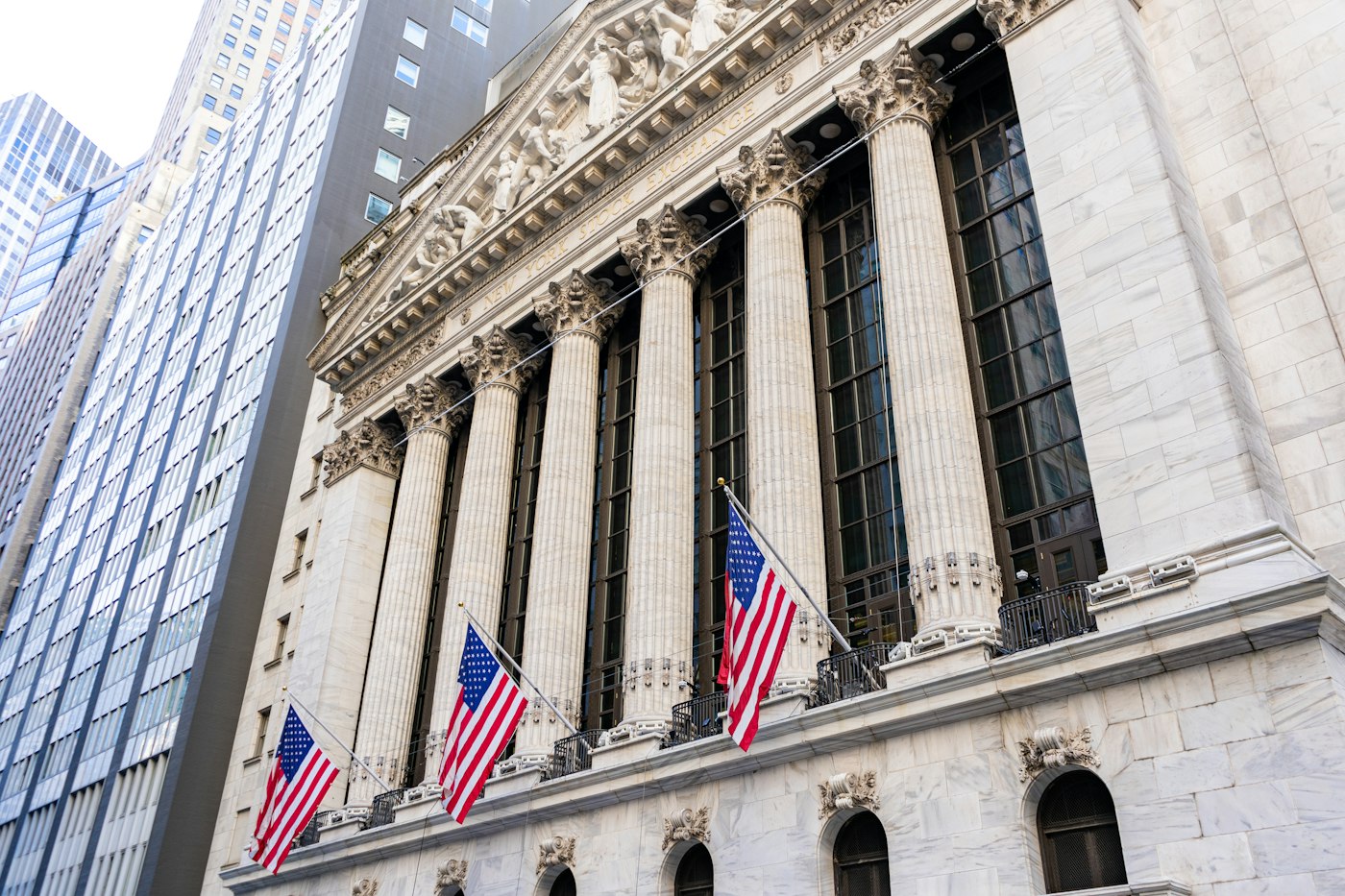The New York Stock Exchange on Wall Street with US flags, in daylight
